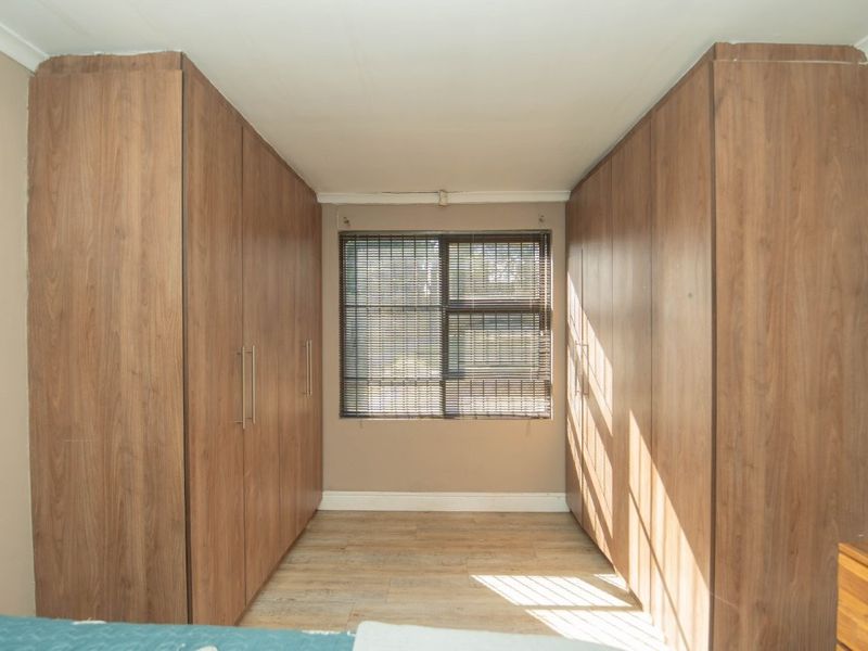 A bedroom featuring extensive floor-to-ceiling built-in wooden cupboards, laminate flooring, and venetian blinds, offering ample storage space.