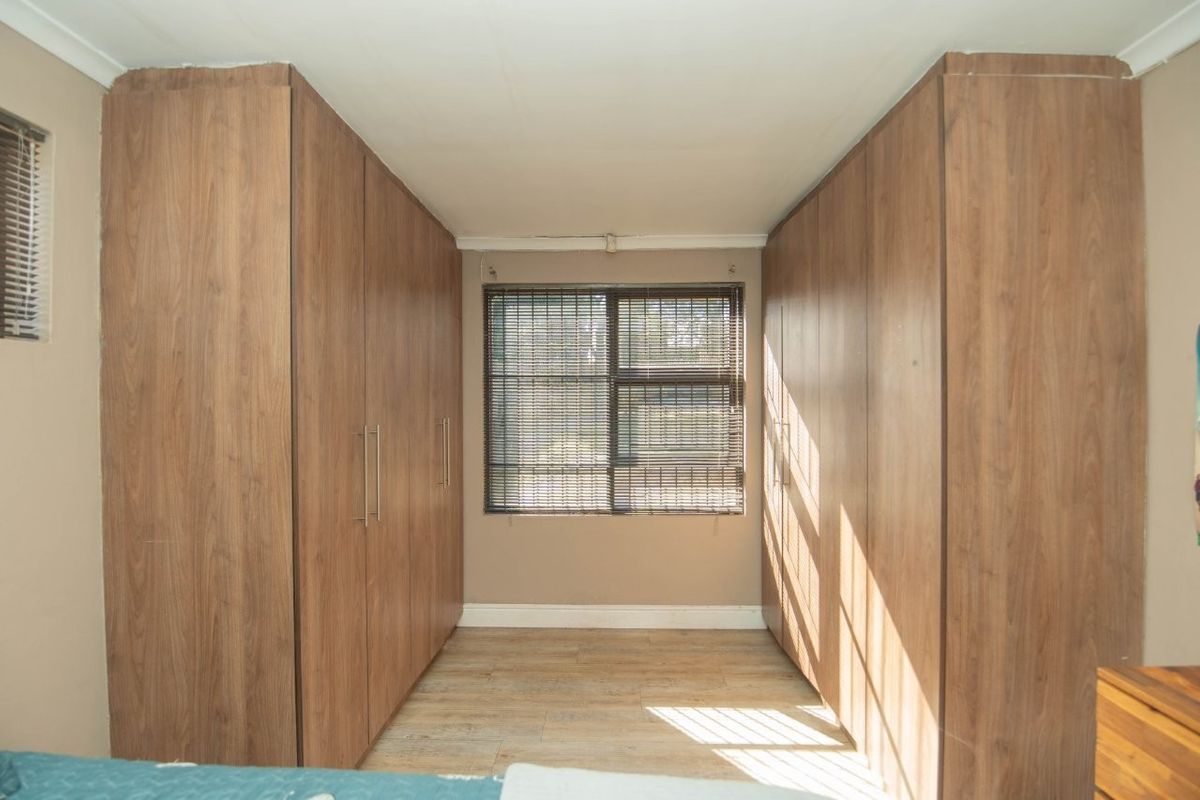 A bedroom featuring extensive floor-to-ceiling built-in wooden cupboards, laminate flooring, and venetian blinds, offering ample storage space.