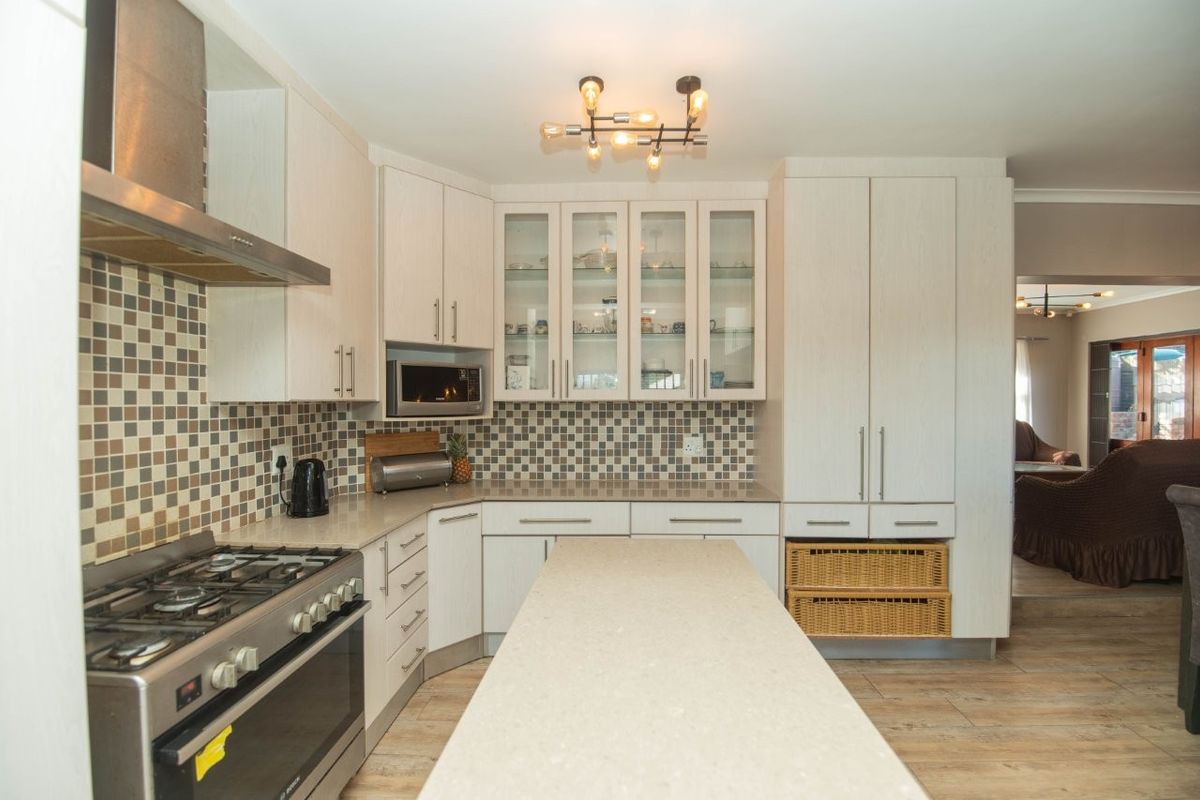 Modern kitchen featuring light wood cabinetry, stone countertops, a gas stove with extractor fan, and a central island with mosaic tile backsplash.