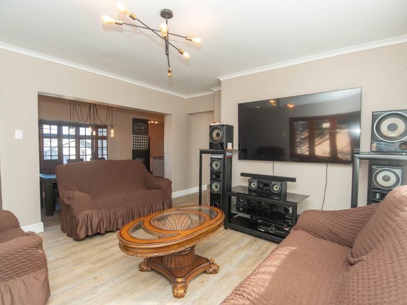 Spacious open-plan living area featuring modern light fixtures and light-toned laminate flooring, seamlessly connecting to the adjacent dining space.
