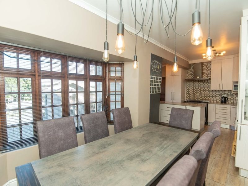 Open-plan dining and kitchen area featuring modern cabinetry, built-in appliances, tiled backsplash, and a large bay window providing natural light.