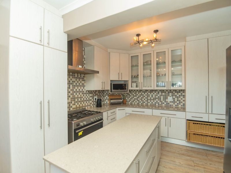 Modern kitchen featuring light wood-grain cabinetry, stone countertops, a central island, mosaic tile backsplash, and integrated stainless steel appliances.