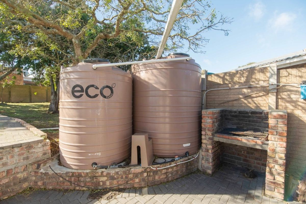 Rear outdoor area featuring two large water storage tanks and a brick built-in braai on a paved patio surface.
