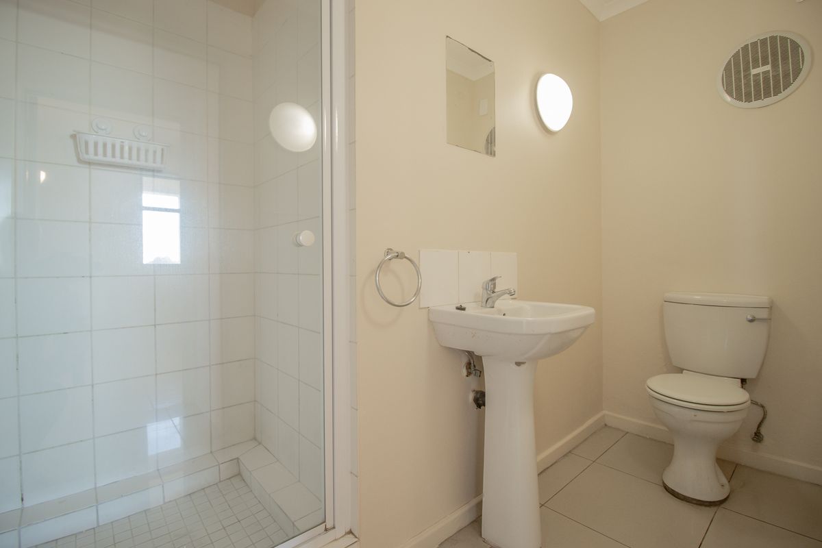 A functional bathroom featuring a pedestal basin, a shower enclosure with glass door, and a standard toilet, finished with neutral wall paint and tiled flooring.