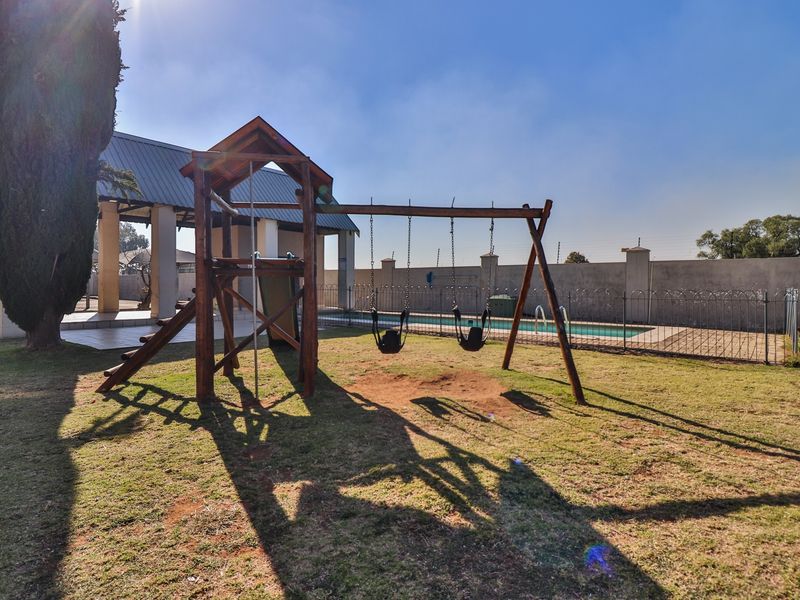 Outdoor recreational area featuring a swimming pool, covered patio space, and a wooden playground set within a fenced garden.