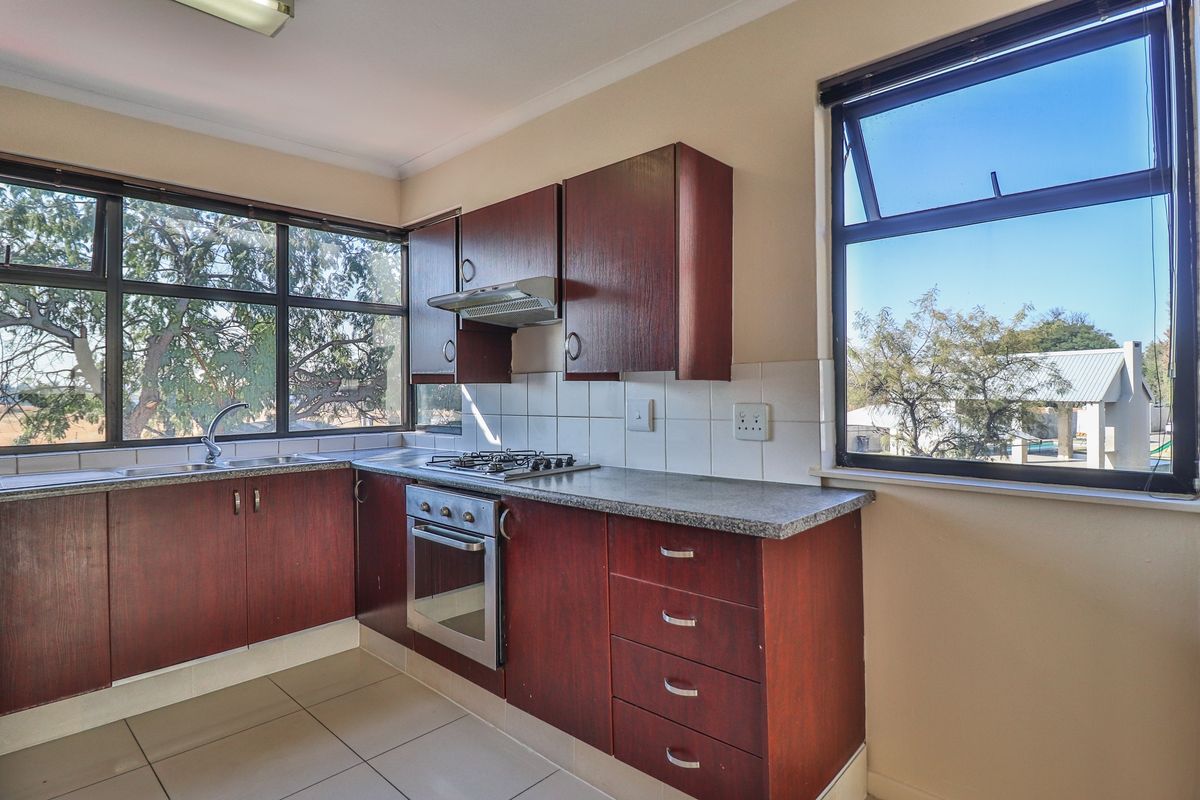 A functional kitchen featuring dark wood cabinetry, granite countertops, a gas hob, built-in oven, and large windows providing ample natural light.