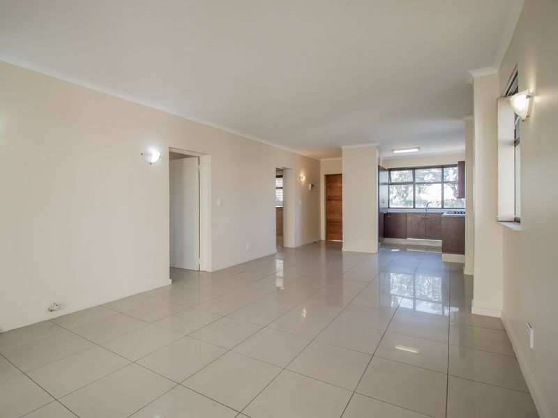 Spacious open-plan living area featuring neutral wall tones, polished porcelain floor tiles, and a functional kitchen with built-in cabinetry.