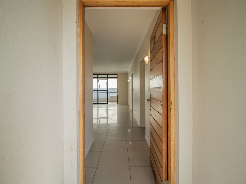 A bright, tiled hallway leading from an entrance door through to an open-plan living area with views of the exterior.