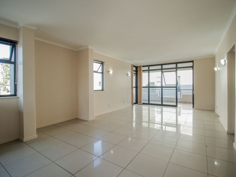 A bright, spacious, and empty living area featuring neutral tiled flooring, modern aluminium window frames, and direct access to an outdoor balcony.