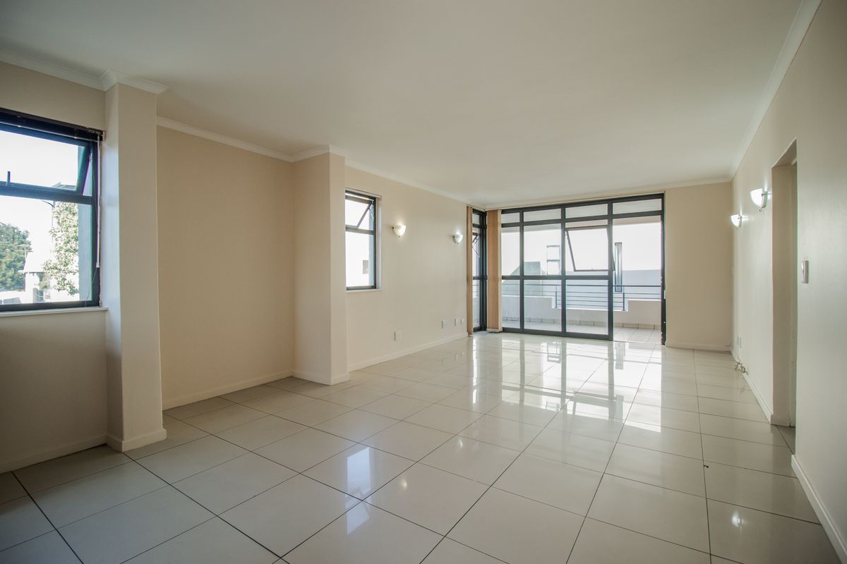 A bright, spacious, and empty living area featuring neutral tiled flooring, modern aluminium window frames, and direct access to an outdoor balcony.