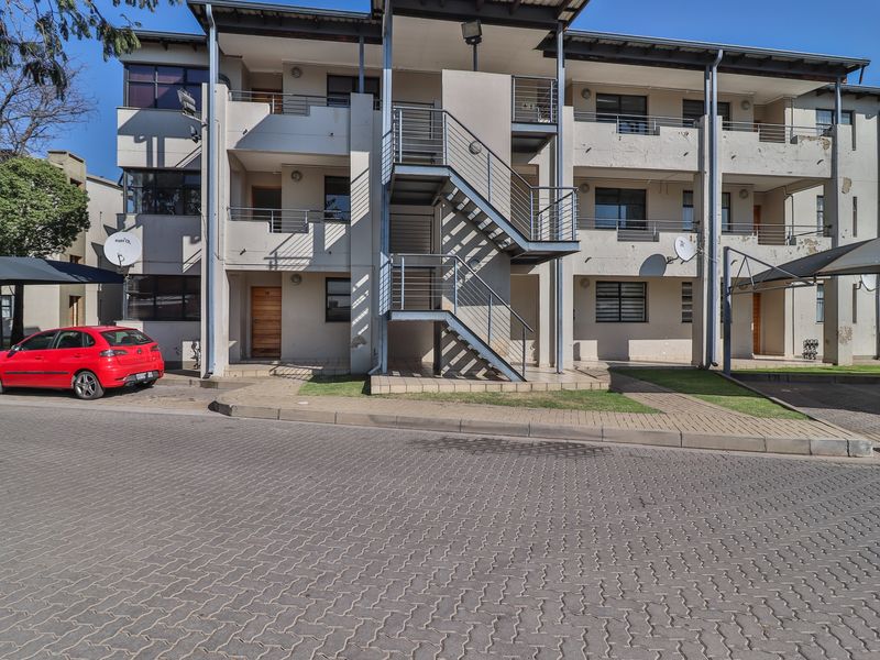 Front elevation of a multi-story apartment complex featuring external steel staircases, paved parking areas, and covered carports.