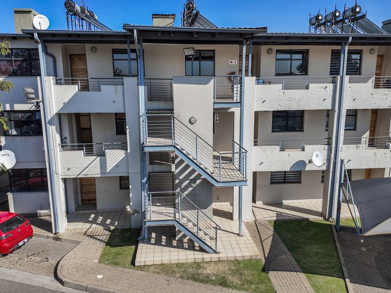 Exterior view of a multi-story apartment complex featuring external staircases, tiled walkways, and roof-mounted solar water heating systems.