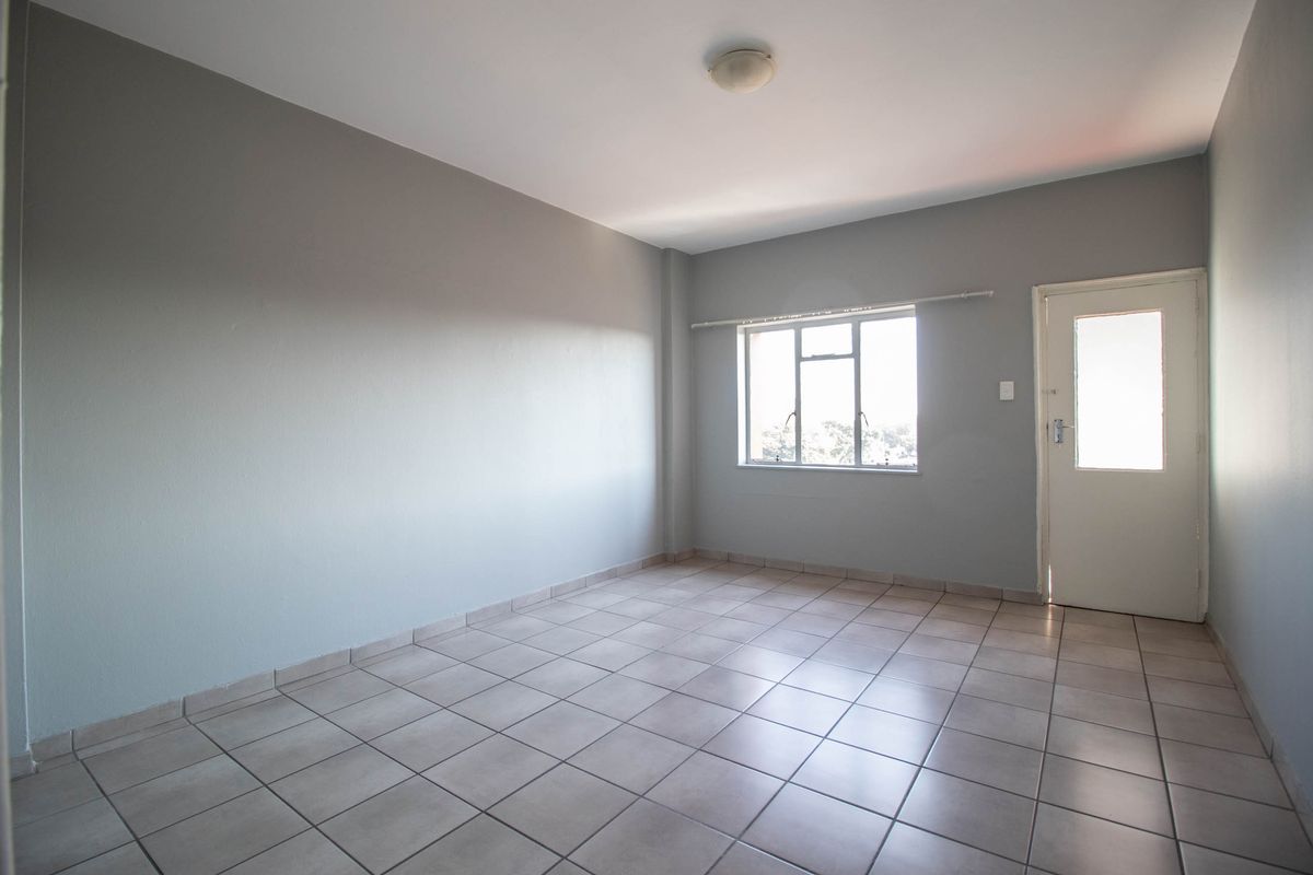A clean, empty bedroom featuring neutral grey walls, tiled flooring, and natural light from a window and adjacent door.