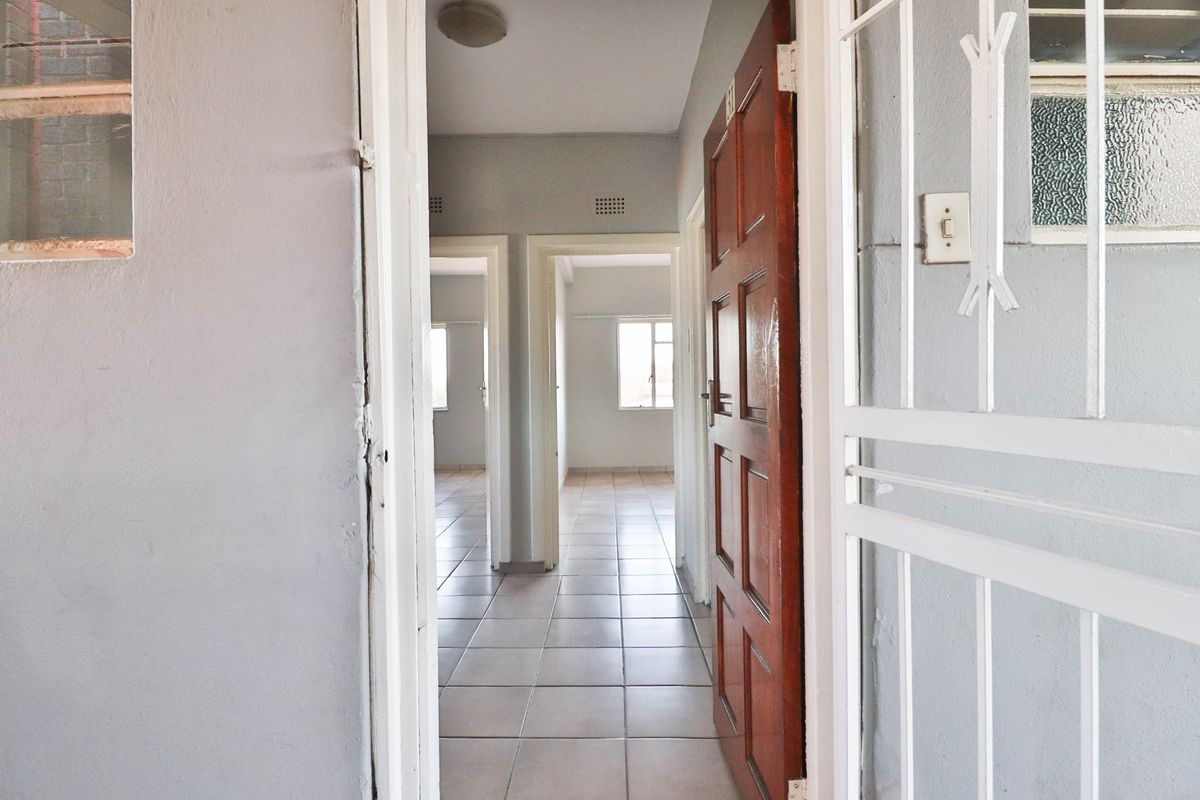 A view through an open timber door into a tiled hallway leading to multiple empty rooms, featuring a security gate and neutral wall finishes.