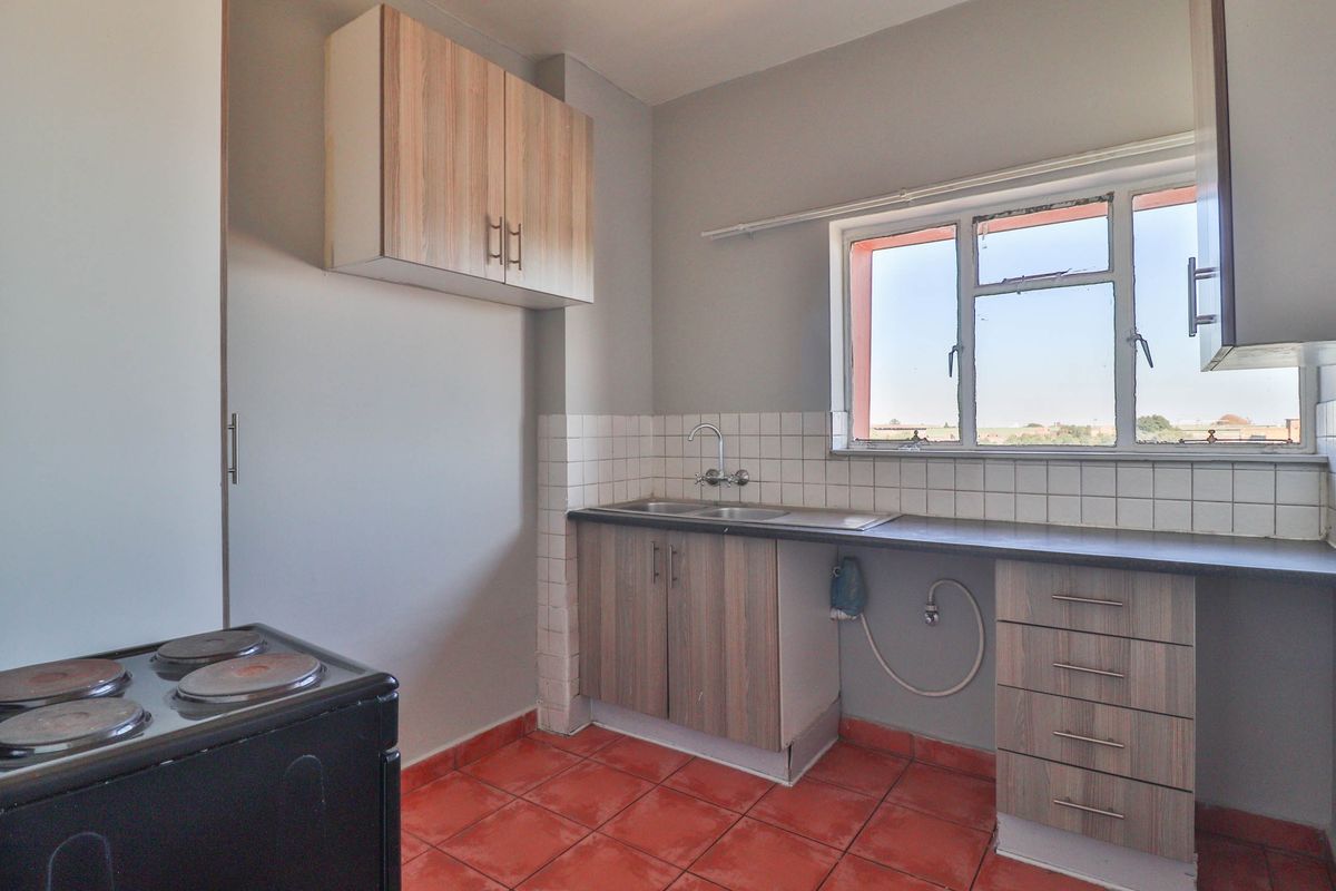 A functional kitchen featuring laminate cabinetry, a stainless steel sink, tiled backsplash, and tiled flooring, offering a blank canvas for potential modern updates.