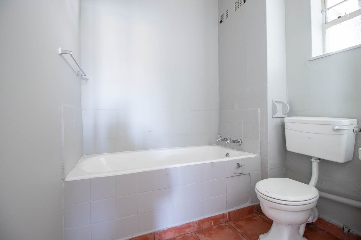 A functional bathroom featuring a standard bathtub, toilet, and tiled flooring, presenting an opportunity for modernization and cosmetic updates.