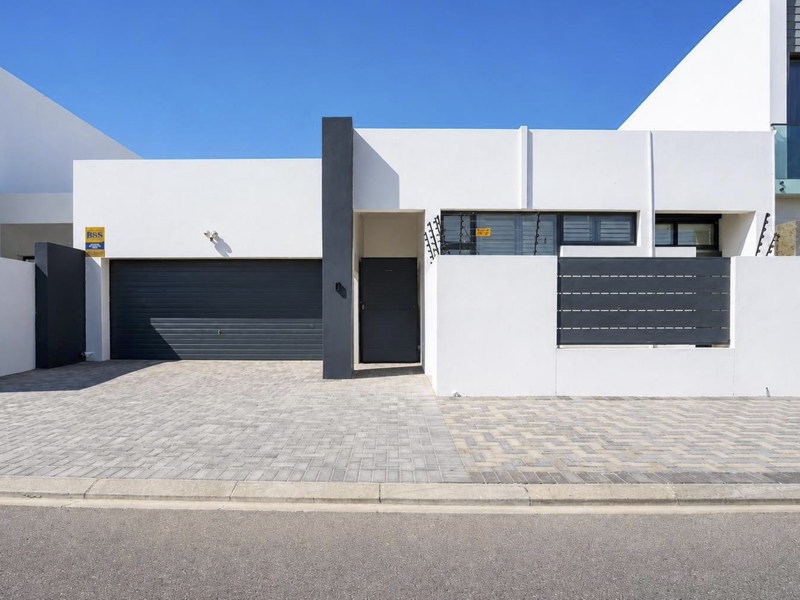 Modern contemporary front facade featuring a paved driveway, secure automated garage, and clean architectural lines with integrated security fencing.
