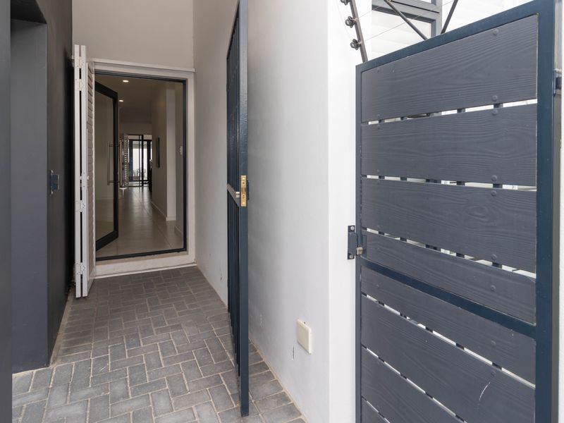 A secure entrance area featuring a paved walkway, modern security gate, and clear access into the main interior living space.