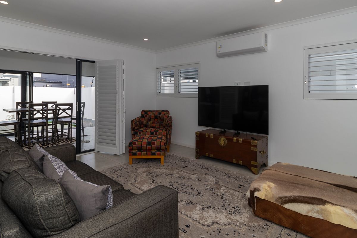 A well-maintained living room featuring split-system air conditioning, louvre shutters, and large sliding glass doors providing seamless access to the outdoor patio area.