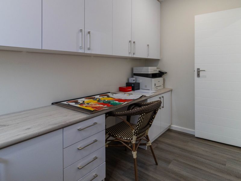A functional home office featuring extensive built-in white cabinetry, a spacious laminate desk surface, and modern wood-look flooring.