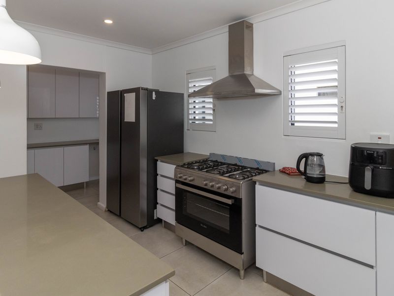 Modern kitchen featuring stone countertops, gas stove with stainless steel extractor, white cabinetry, and plantation shutters, with an adjacent scullery area.