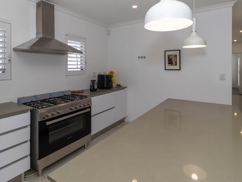 Modern kitchen featuring a large stone island, stainless steel gas stove with extractor fan, white cabinetry, and plantation shutters.