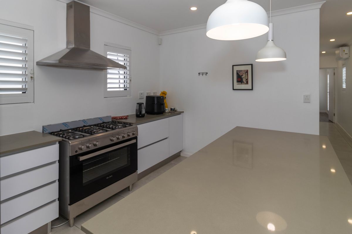 Modern kitchen featuring a large stone island, stainless steel gas stove with extractor fan, white cabinetry, and plantation shutters.