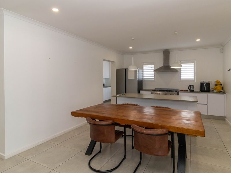 Open-plan kitchen and dining area featuring a central island, stainless steel extractor fan, gas cooktop, tiled flooring, and modern recessed lighting.