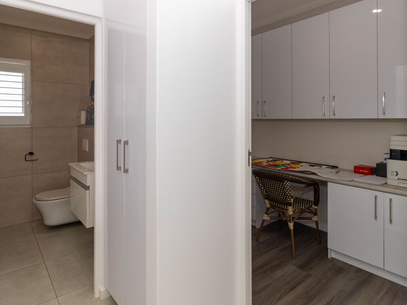 A hallway view showing a modern bathroom with tiled finishes and an adjacent office space featuring built-in white cabinetry and desk area.
