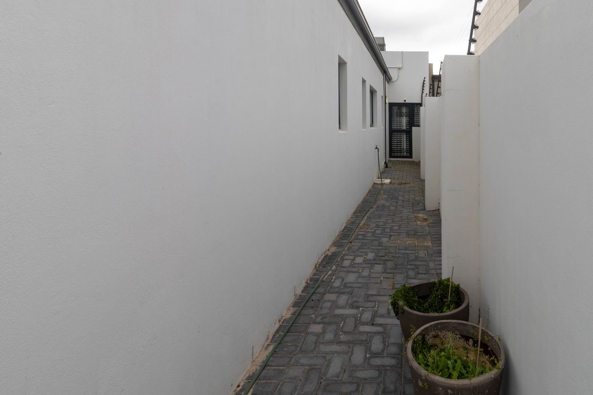 A narrow paved side passage featuring white rendered walls, an external tap, and a secure gate at the end.