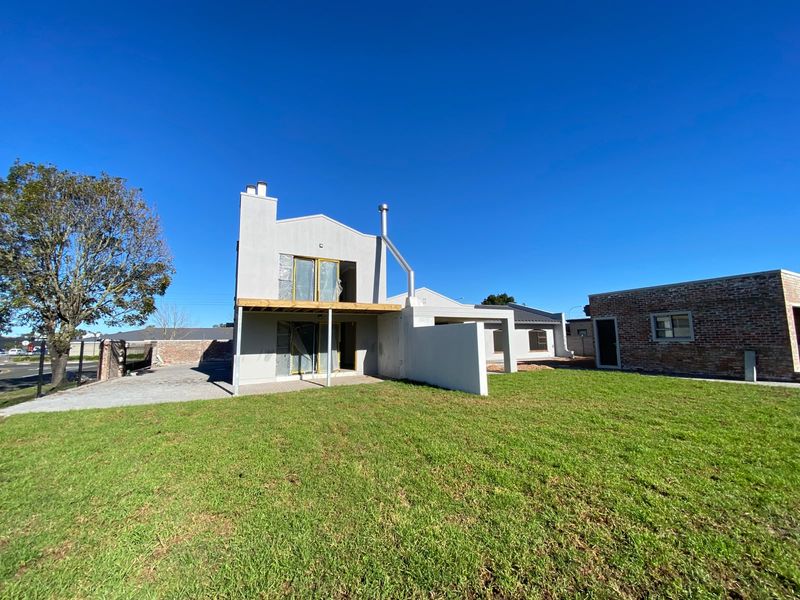 Rear view of a modern house featuring a balcony, patio area, and a separate brick outbuilding set within a spacious lawn.