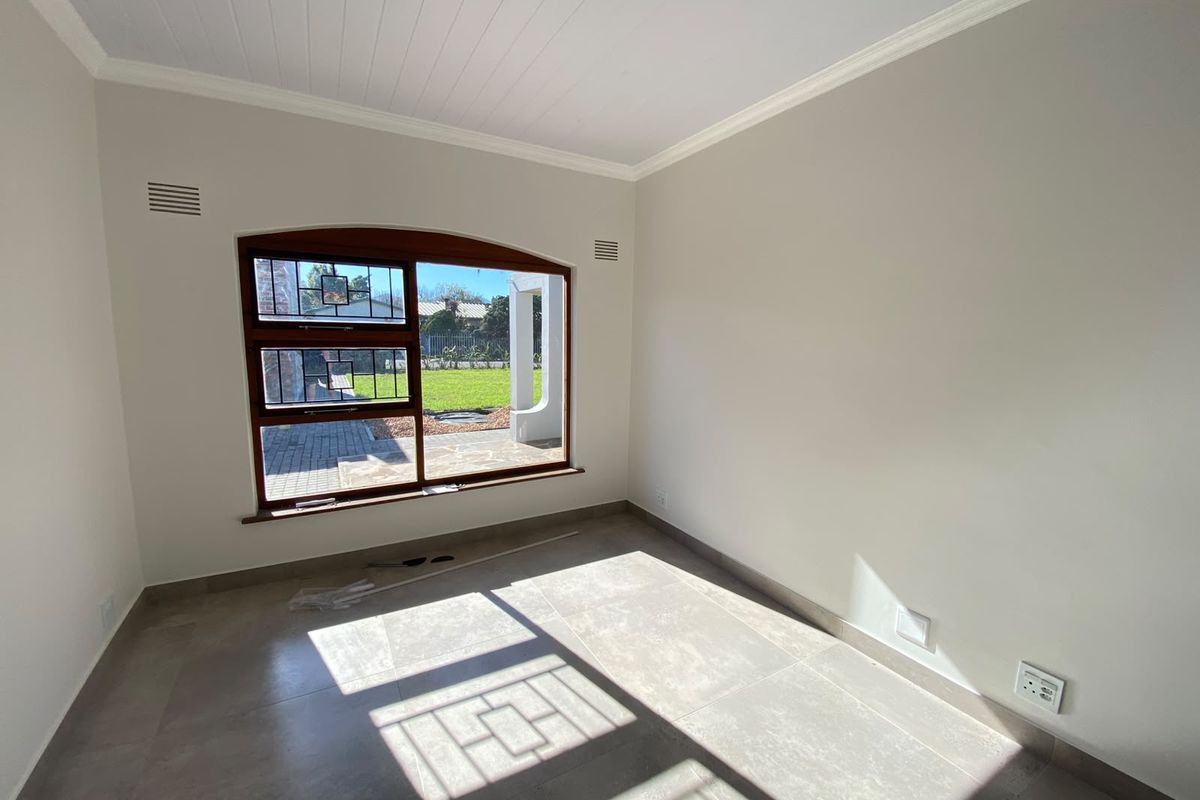 A bright, empty bedroom featuring neutral wall tones, large timber-framed windows with security bars, and modern tiled flooring.