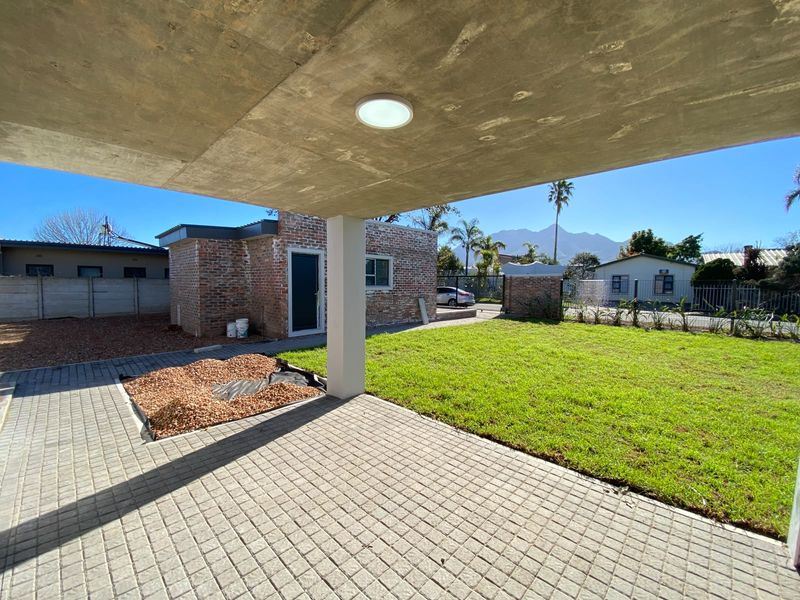 A covered concrete patio overlooking a private garden with brick exterior walls and mountain views in the distance.