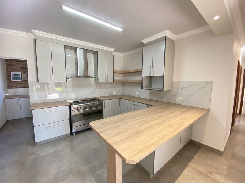Modern kitchen featuring light grey cabinetry, wooden countertops, a breakfast bar, and a gas stove with a stainless steel extractor fan.