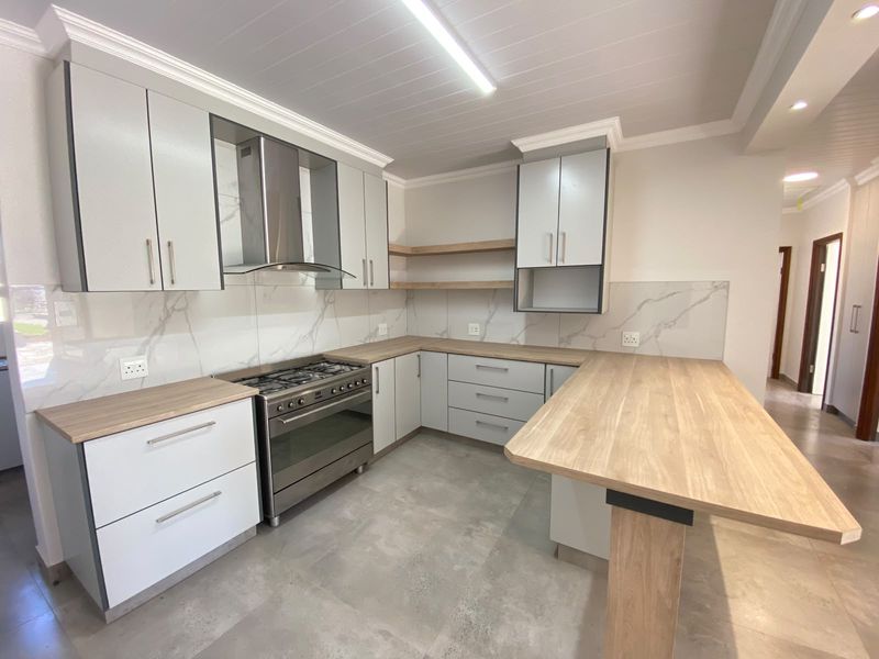 Modern kitchen featuring light grey cabinetry, timber-look countertops, a gas stove with extractor fan, and marble-effect splashbacks with a breakfast bar.