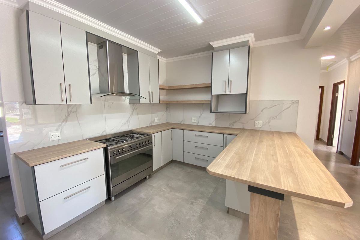 Modern kitchen featuring light grey cabinetry, timber-look countertops, a gas stove with extractor fan, and marble-effect splashbacks with a breakfast bar.