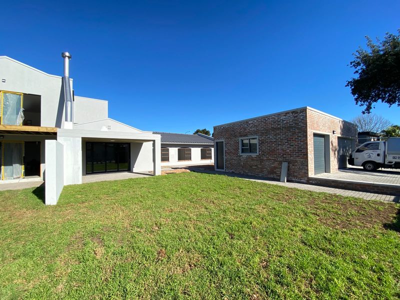 Rear view of the property featuring a lawn, covered patio, and a detached exposed brick garage under construction.