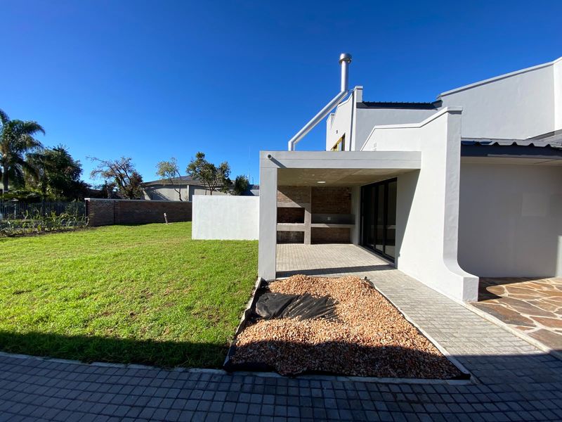 Covered patio area featuring a built-in braai, chimney flue, and direct access to the rear garden through sliding glass doors.