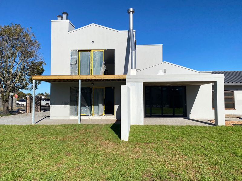 Rear view of a modern house featuring a patio, balcony, and external chimney, currently undergoing final construction and finishing touches.