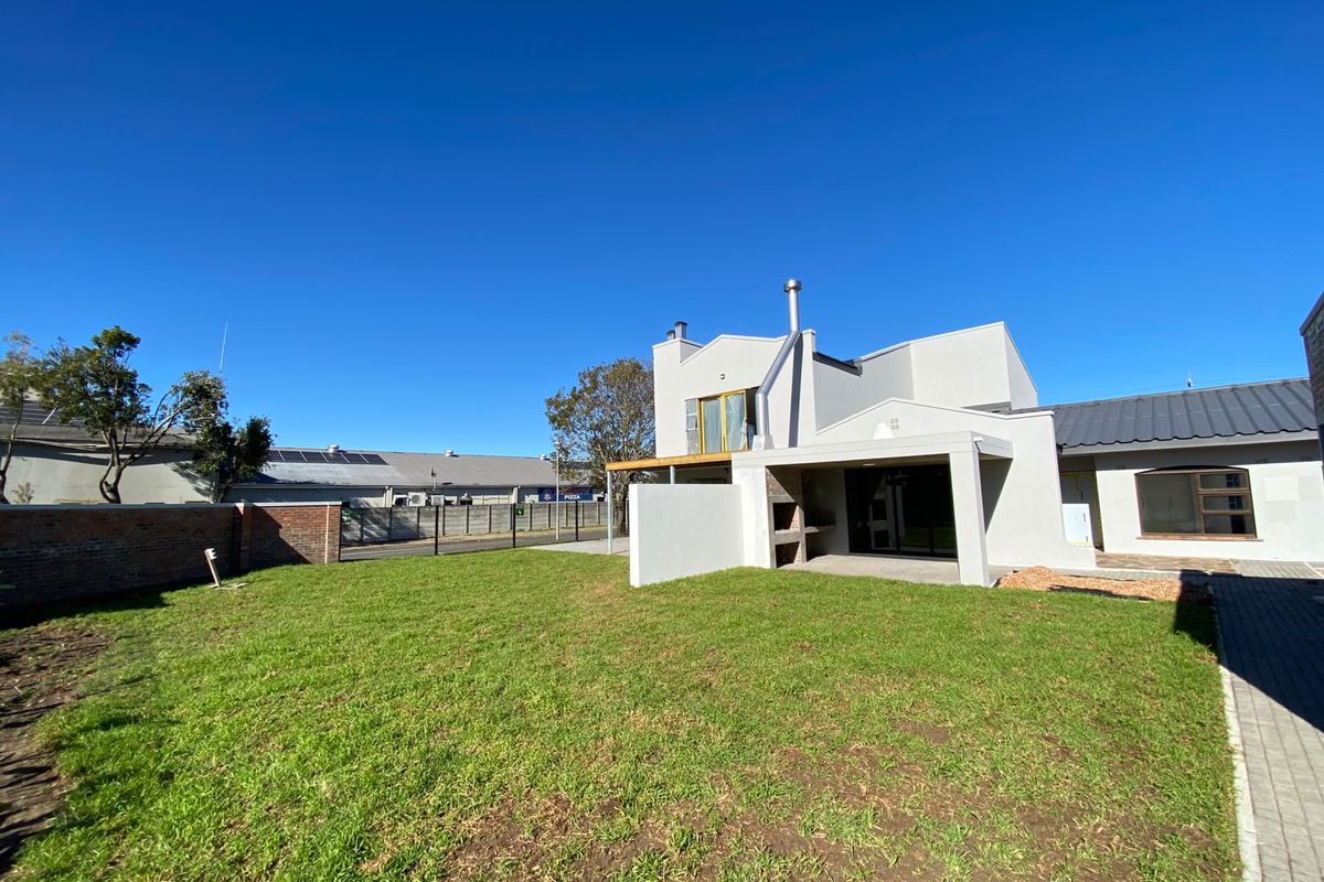 Rear view of the property featuring a spacious lawn, a covered patio with a built-in braai, and a secure brick boundary wall.
