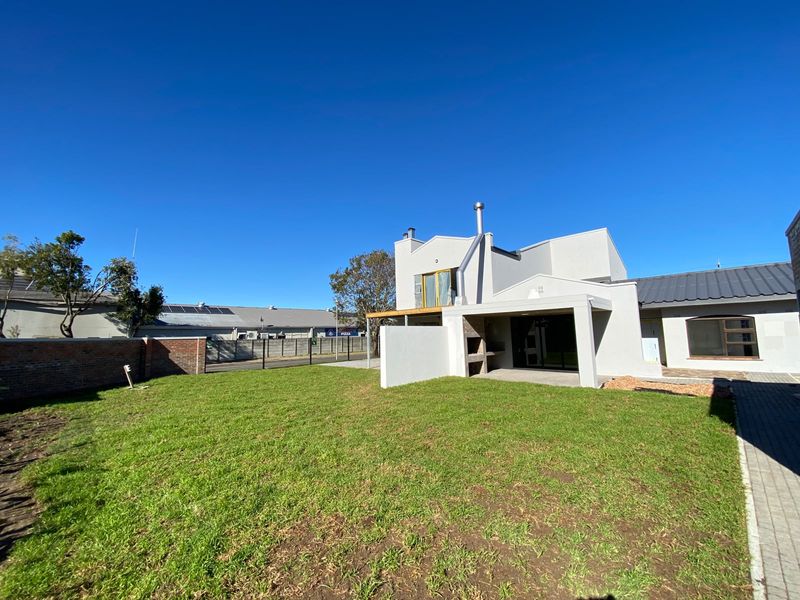 Rear view of the property featuring a spacious lawn, a covered patio with a built-in braai, and a secure brick boundary wall.