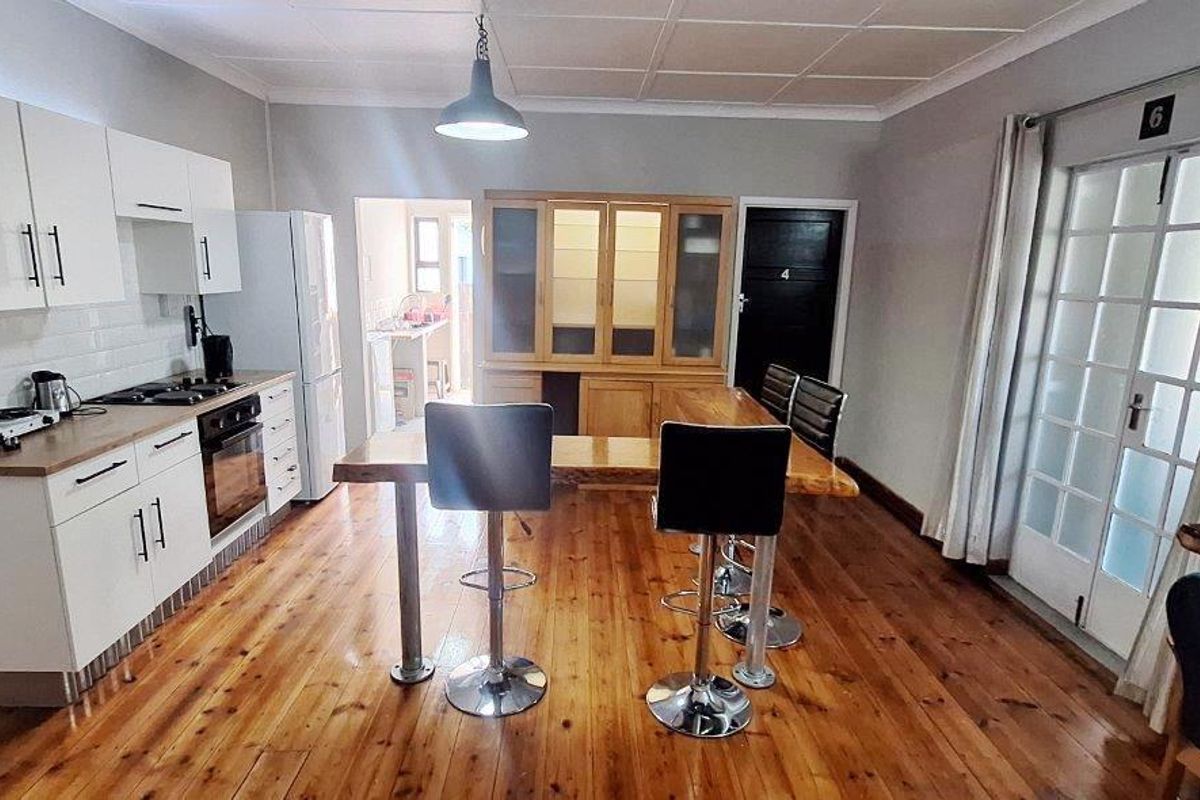 Open-plan kitchen and dining area featuring timber flooring, white cabinetry, subway tile backsplash, and direct access to an outdoor space via french doors.