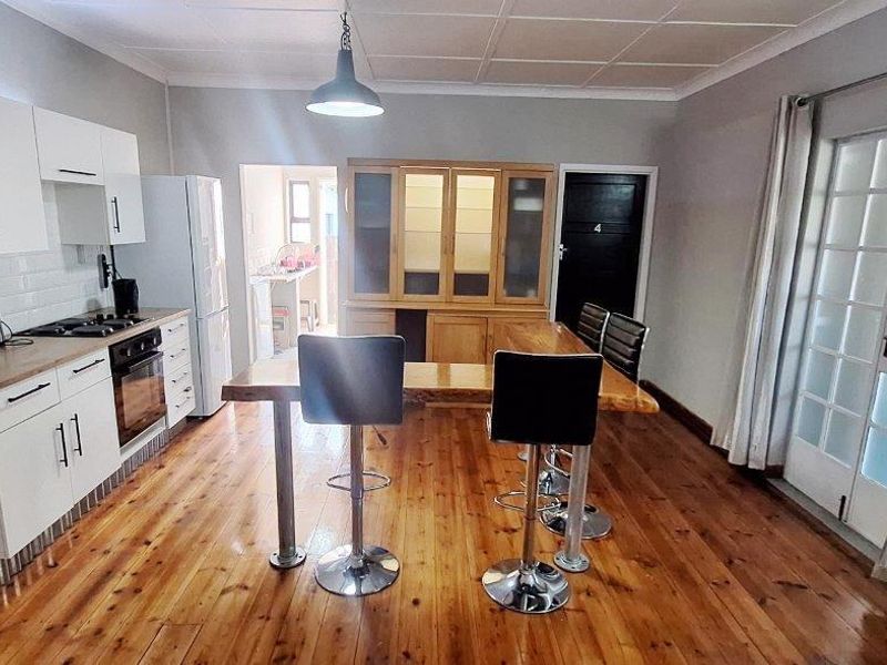 Open-plan kitchen and dining area featuring timber flooring, white cabinetry, subway tile backsplash, and direct access to an outdoor space via french doors.