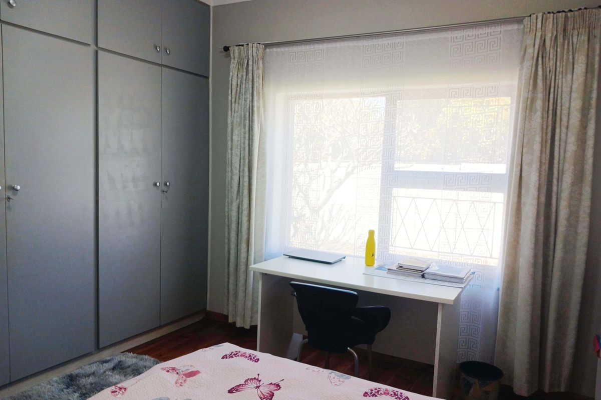 A well-maintained bedroom featuring ample built-in cupboard storage, laminate flooring, and a large window allowing for natural light.