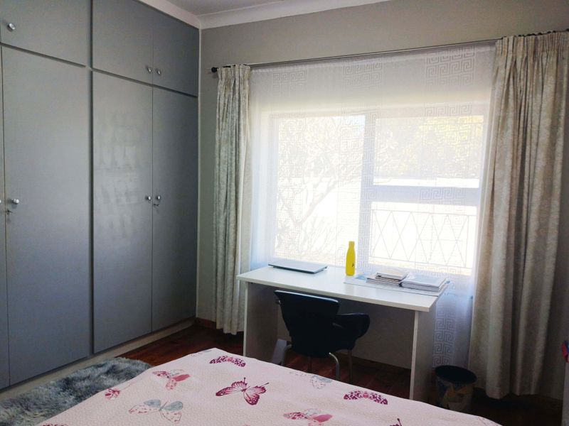 A well-maintained bedroom featuring ample built-in cupboard storage, laminate flooring, and a large window allowing for natural light.