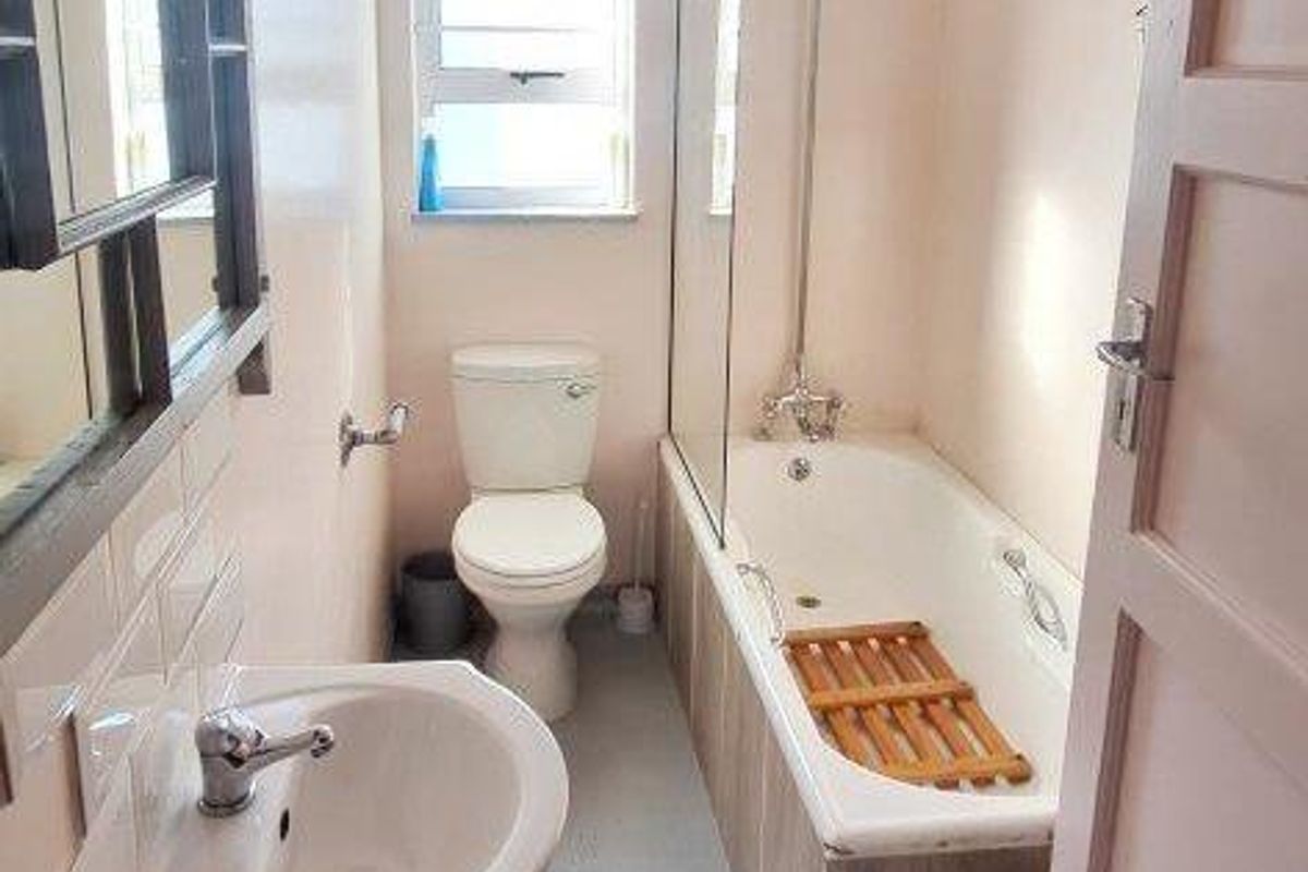 A functional bathroom featuring a pedestal sink, toilet, and a bathtub with a glass shower screen and overhead shower fixture.