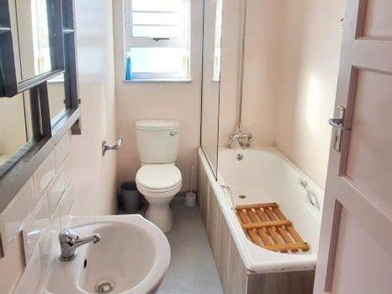 A functional bathroom featuring a pedestal sink, toilet, and a bathtub with a glass shower screen and overhead shower fixture.