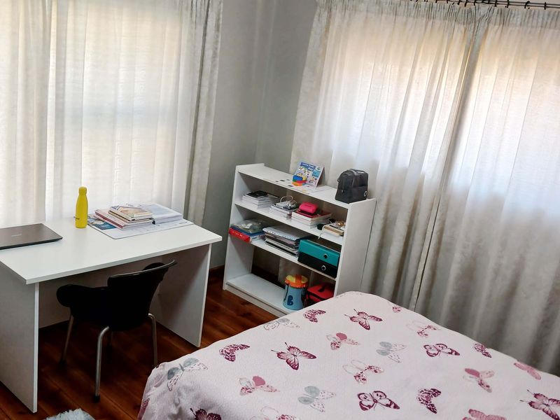 A functional bedroom featuring timber flooring and dual window treatments, providing a comfortable space with natural light.
