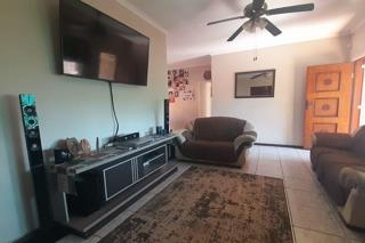 A living room featuring tiled flooring, a ceiling fan, and a wooden entrance door, providing a functional and comfortable living space.