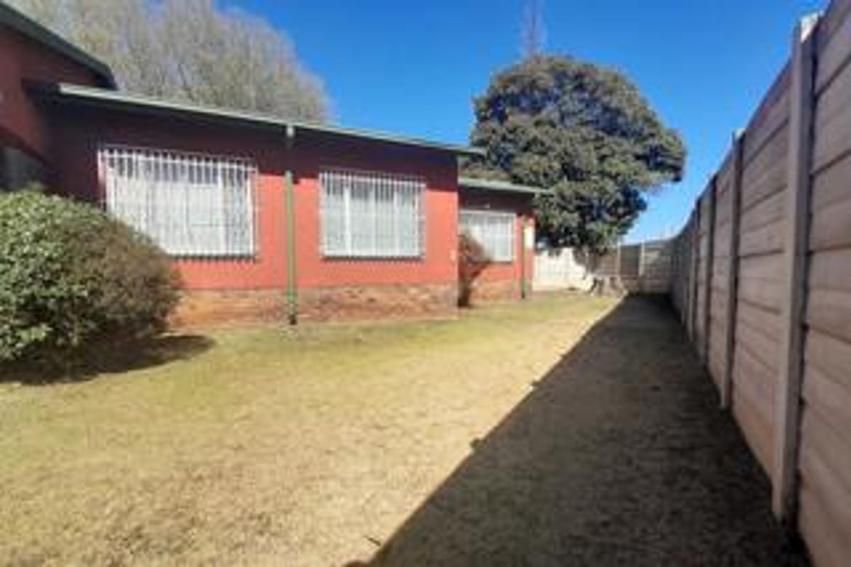 Rear exterior view of the house featuring a brick facade, security bars on windows, and a private garden area enclosed by a precast concrete wall.
